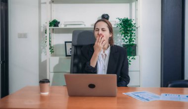Geç saatlere kadar masa başında çalışırken ofis sendromu geçiren yorgun ve stresli bir iş kadını. Uzun saatler ve aşırı ekran süresi uzun çalışma saatlerinden dolayı fiziksel ve zihinsel yorgunluğa yol açar..