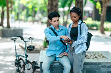 Üniversite öğrencileri iş projelerini tartışıyor. Bisiklet ve elektrikli scooter yakınlarda park edilmiş. Çevre dostu bir yol izlenimi uyandırıyor. Teknoloji ve sürdürülebilir ulaşım ile modern öğrenci yaşam tarzı