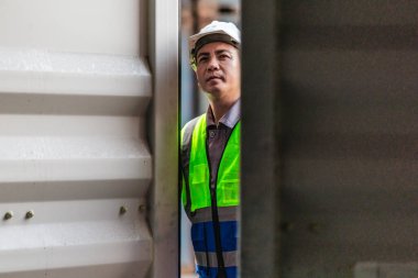 Bir nakliye tesisinde konteynır teftişi yapan sanayi işçileri. Belgelerin incelenmesi ve lojistik, ulaşım ve kargo yönetiminde doğruluğu sağlamak için el bilgisayarı kullanılması.