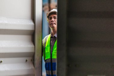 Bir nakliye tesisinde konteynır teftişi yapan sanayi işçileri. Belgelerin incelenmesi ve lojistik, ulaşım ve kargo yönetiminde doğruluğu sağlamak için el bilgisayarı kullanılması.