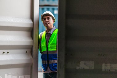 Bir nakliye tesisinde konteynır teftişi yapan sanayi işçileri. Belgelerin incelenmesi ve lojistik, ulaşım ve kargo yönetiminde doğruluğu sağlamak için el bilgisayarı kullanılması.