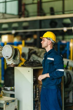 Fabrika teknisyeni, endüstriyel tesisin içindeki robotik kolda mekanik bakım yapıyor. Modern imalat ortamlarında hassas mühendislik, güvenlik protokolleri ve otomasyonun altını çizmek