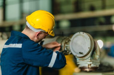 Fabrika teknisyeni, endüstriyel tesisin içindeki robotik kolda mekanik bakım yapıyor. Modern imalat ortamlarında hassas mühendislik, güvenlik protokolleri ve otomasyonun altını çizmek