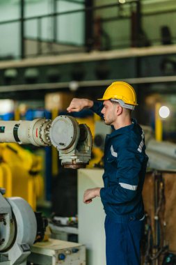 Fabrika teknisyeni, endüstriyel tesisin içindeki robotik kolda mekanik bakım yapıyor. Modern imalat ortamlarında hassas mühendislik, güvenlik protokolleri ve otomasyonun altını çizmek
