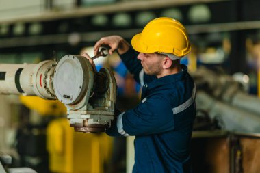 Fabrika teknisyeni, endüstriyel tesisin içindeki robotik kolda mekanik bakım yapıyor. Modern imalat ortamlarında hassas mühendislik, güvenlik protokolleri ve otomasyonun altını çizmek