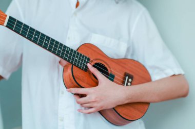 Kıvırcık saçlı Asyalı bir kadın açık hava ortamında ukulele çalıyor, mutluluk ve müzik enerjisi saçıyor. Doğal ve mimari unsurlara sahip rahat ve sanatsal bir ortam.