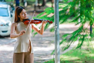 Genç bir Asyalı kadın bereketli yeşilliklerle çevrili huzurlu bir açık hava ortamında kibarca keman çalıyor. Doğada bir müzik konsantrasyonu ve sükunet anı yakalıyorum..