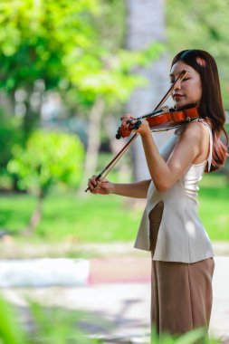 Genç bir Asyalı kadın bereketli yeşilliklerle çevrili huzurlu bir açık hava ortamında kibarca keman çalıyor. Doğada bir müzik konsantrasyonu ve sükunet anı yakalıyorum..