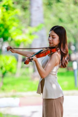Genç bir Asyalı kadın bereketli yeşilliklerle çevrili huzurlu bir açık hava ortamında kibarca keman çalıyor. Doğada bir müzik konsantrasyonu ve sükunet anı yakalıyorum..