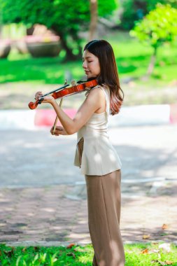 Genç bir Asyalı kadın bereketli yeşilliklerle çevrili huzurlu bir açık hava ortamında kibarca keman çalıyor. Doğada bir müzik konsantrasyonu ve sükunet anı yakalıyorum..