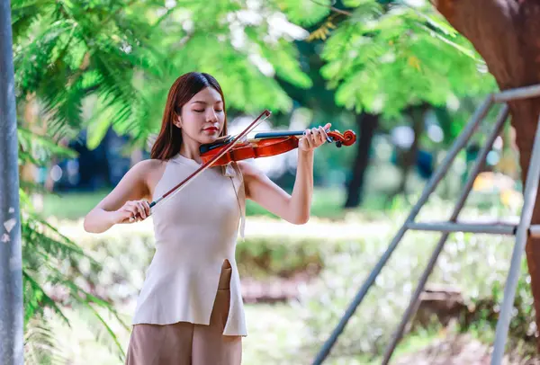 Genç bir Asyalı kadın bereketli yeşilliklerle çevrili huzurlu bir açık hava ortamında kibarca keman çalıyor. Doğada bir müzik konsantrasyonu ve sükunet anı yakalıyorum..