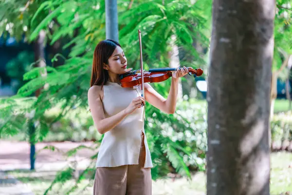 Genç bir Asyalı kadın bereketli yeşilliklerle çevrili huzurlu bir açık hava ortamında kibarca keman çalıyor. Doğada bir müzik konsantrasyonu ve sükunet anı yakalıyorum..