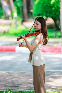 Genç bir Asyalı kadın bereketli yeşilliklerle çevrili huzurlu bir açık hava ortamında kibarca keman çalıyor. Doğada bir müzik konsantrasyonu ve sükunet anı yakalıyorum..