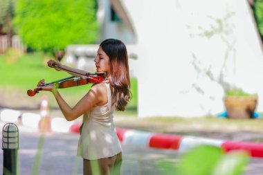 Genç bir Asyalı kadın bereketli yeşilliklerle çevrili huzurlu bir açık hava ortamında kibarca keman çalıyor. Doğada bir müzik konsantrasyonu ve sükunet anı yakalıyorum..
