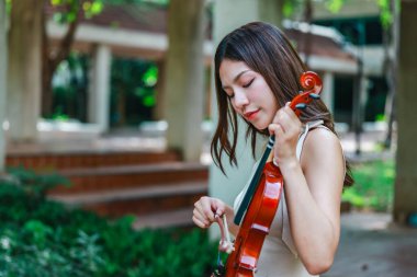 Genç bir Asyalı kadın bereketli yeşilliklerle çevrili huzurlu bir açık hava ortamında kibarca keman çalıyor. Doğada bir müzik konsantrasyonu ve sükunet anı yakalıyorum..