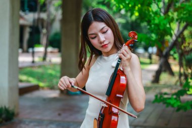 Genç bir Asyalı kadın bereketli yeşilliklerle çevrili huzurlu bir açık hava ortamında kibarca keman çalıyor. Doğada bir müzik konsantrasyonu ve sükunet anı yakalıyorum..