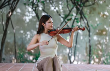 Genç bir Asyalı kadın bereketli yeşilliklerle çevrili huzurlu bir açık hava ortamında kibarca keman çalıyor. Doğada bir müzik konsantrasyonu ve sükunet anı yakalıyorum..