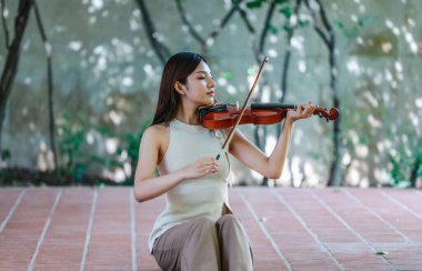 Genç bir Asyalı kadın bereketli yeşilliklerle çevrili huzurlu bir açık hava ortamında kibarca keman çalıyor. Doğada bir müzik konsantrasyonu ve sükunet anı yakalıyorum..