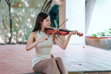 Genç bir Asyalı kadın bereketli yeşilliklerle çevrili huzurlu bir açık hava ortamında kibarca keman çalıyor. Doğada bir müzik konsantrasyonu ve sükunet anı yakalıyorum..