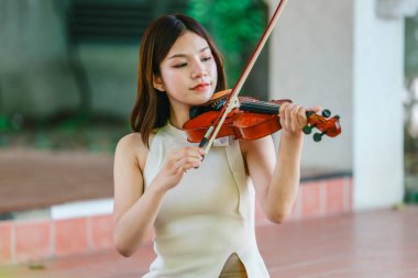 Genç bir Asyalı kadın bereketli yeşilliklerle çevrili huzurlu bir açık hava ortamında kibarca keman çalıyor. Doğada bir müzik konsantrasyonu ve sükunet anı yakalıyorum..