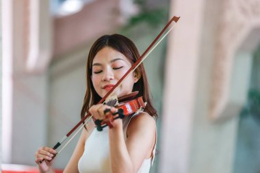 Genç bir Asyalı kadın bereketli yeşilliklerle çevrili huzurlu bir açık hava ortamında kibarca keman çalıyor. Doğada bir müzik konsantrasyonu ve sükunet anı yakalıyorum..