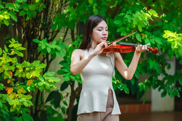 Genç bir Asyalı kadın bereketli yeşilliklerle çevrili huzurlu bir açık hava ortamında kibarca keman çalıyor. Doğada bir müzik konsantrasyonu ve sükunet anı yakalıyorum..