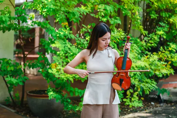 Genç bir Asyalı kadın bereketli yeşilliklerle çevrili huzurlu bir açık hava ortamında kibarca keman çalıyor. Doğada bir müzik konsantrasyonu ve sükunet anı yakalıyorum..