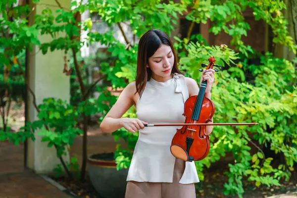 Genç bir Asyalı kadın bereketli yeşilliklerle çevrili huzurlu bir açık hava ortamında kibarca keman çalıyor. Doğada bir müzik konsantrasyonu ve sükunet anı yakalıyorum..