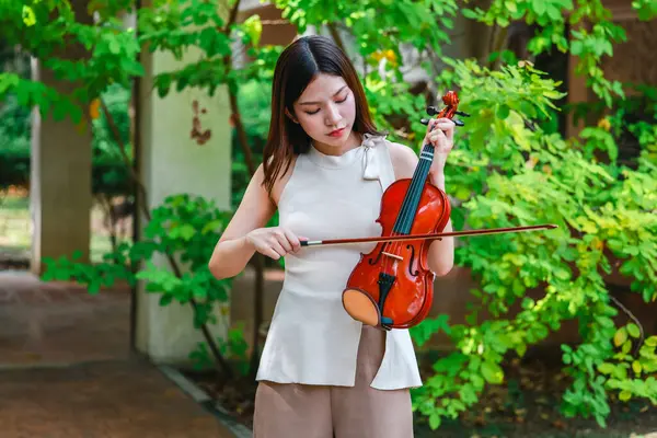 Genç bir Asyalı kadın bereketli yeşilliklerle çevrili huzurlu bir açık hava ortamında kibarca keman çalıyor. Doğada bir müzik konsantrasyonu ve sükunet anı yakalıyorum..