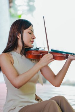 Genç bir Asyalı kadın bereketli yeşilliklerle çevrili huzurlu bir açık hava ortamında kibarca keman çalıyor. Doğada bir müzik konsantrasyonu ve sükunet anı yakalıyorum..