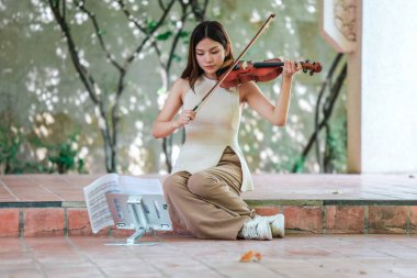 Genç bir Asyalı kadın bereketli yeşilliklerle çevrili huzurlu bir açık hava ortamında kibarca keman çalıyor. Doğada bir müzik konsantrasyonu ve sükunet anı yakalıyorum..