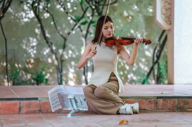 Genç bir Asyalı kadın bereketli yeşilliklerle çevrili huzurlu bir açık hava ortamında kibarca keman çalıyor. Doğada bir müzik konsantrasyonu ve sükunet anı yakalıyorum..