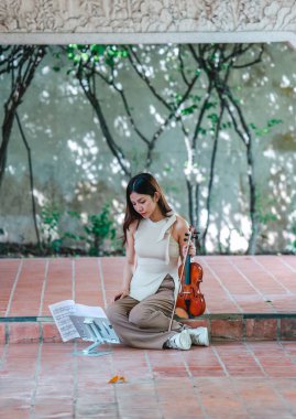 Genç bir Asyalı kadın bereketli yeşilliklerle çevrili huzurlu bir açık hava ortamında kibarca keman çalıyor. Doğada bir müzik konsantrasyonu ve sükunet anı yakalıyorum..