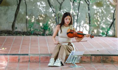 Genç bir Asyalı kadın bereketli yeşilliklerle çevrili huzurlu bir açık hava ortamında kibarca keman çalıyor. Doğada bir müzik konsantrasyonu ve sükunet anı yakalıyorum..