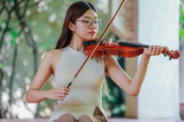 Genç bir Asyalı kadın bereketli yeşilliklerle çevrili huzurlu bir açık hava ortamında kibarca keman çalıyor. Doğada bir müzik konsantrasyonu ve sükunet anı yakalıyorum..