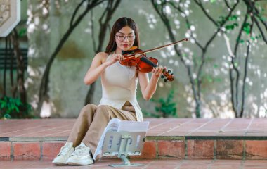 Genç bir Asyalı kadın bereketli yeşilliklerle çevrili huzurlu bir açık hava ortamında kibarca keman çalıyor. Doğada bir müzik konsantrasyonu ve sükunet anı yakalıyorum..