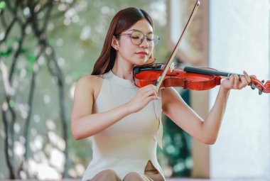 Genç bir Asyalı kadın bereketli yeşilliklerle çevrili huzurlu bir açık hava ortamında kibarca keman çalıyor. Doğada bir müzik konsantrasyonu ve sükunet anı yakalıyorum..