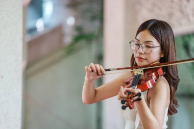 Genç bir Asyalı kadın bereketli yeşilliklerle çevrili huzurlu bir açık hava ortamında kibarca keman çalıyor. Doğada bir müzik konsantrasyonu ve sükunet anı yakalıyorum..