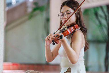 Genç bir Asyalı kadın bereketli yeşilliklerle çevrili huzurlu bir açık hava ortamında kibarca keman çalıyor. Doğada bir müzik konsantrasyonu ve sükunet anı yakalıyorum..