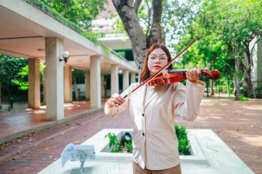 Genç bir Asyalı kadın bereketli yeşilliklerle çevrili huzurlu bir açık hava ortamında kibarca keman çalıyor. Doğada bir müzik konsantrasyonu ve sükunet anı yakalıyorum..