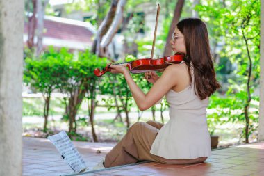 Genç bir Asyalı kadın bereketli yeşilliklerle çevrili huzurlu bir açık hava ortamında kibarca keman çalıyor. Doğada bir müzik konsantrasyonu ve sükunet anı yakalıyorum..