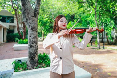 Genç bir Asyalı kadın bereketli yeşilliklerle çevrili huzurlu bir açık hava ortamında kibarca keman çalıyor. Doğada bir müzik konsantrasyonu ve sükunet anı yakalıyorum..