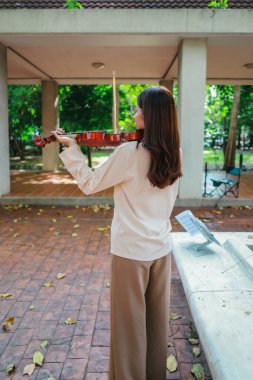 Genç bir Asyalı kadın bereketli yeşilliklerle çevrili huzurlu bir açık hava ortamında kibarca keman çalıyor. Doğada bir müzik konsantrasyonu ve sükunet anı yakalıyorum..