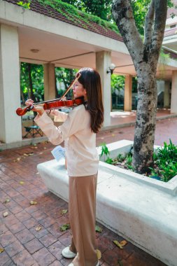 Genç bir Asyalı kadın bereketli yeşilliklerle çevrili huzurlu bir açık hava ortamında kibarca keman çalıyor. Doğada bir müzik konsantrasyonu ve sükunet anı yakalıyorum..