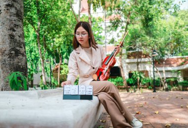 Genç bir Asyalı kadın bereketli yeşilliklerle çevrili huzurlu bir açık hava ortamında kibarca keman çalıyor. Doğada bir müzik konsantrasyonu ve sükunet anı yakalıyorum..