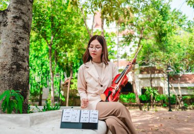 Genç bir Asyalı kadın bereketli yeşilliklerle çevrili huzurlu bir açık hava ortamında kibarca keman çalıyor. Doğada bir müzik konsantrasyonu ve sükunet anı yakalıyorum..