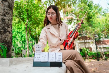 Genç bir Asyalı kadın bereketli yeşilliklerle çevrili huzurlu bir açık hava ortamında kibarca keman çalıyor. Doğada bir müzik konsantrasyonu ve sükunet anı yakalıyorum..