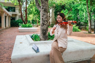 Genç bir Asyalı kadın bereketli yeşilliklerle çevrili huzurlu bir açık hava ortamında kibarca keman çalıyor. Doğada bir müzik konsantrasyonu ve sükunet anı yakalıyorum..