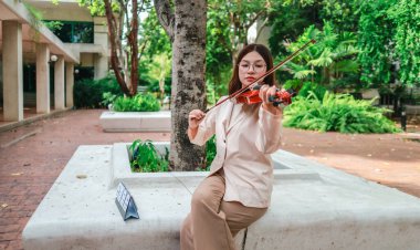 Genç bir Asyalı kadın bereketli yeşilliklerle çevrili huzurlu bir açık hava ortamında kibarca keman çalıyor. Doğada bir müzik konsantrasyonu ve sükunet anı yakalıyorum..