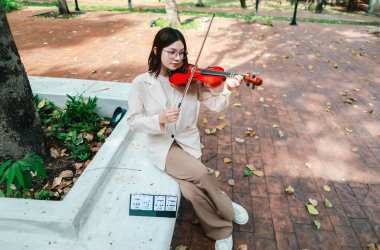 Genç bir Asyalı kadın bereketli yeşilliklerle çevrili huzurlu bir açık hava ortamında kibarca keman çalıyor. Doğada bir müzik konsantrasyonu ve sükunet anı yakalıyorum..